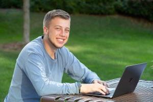 Student smiling and doing work on a laptop outside.