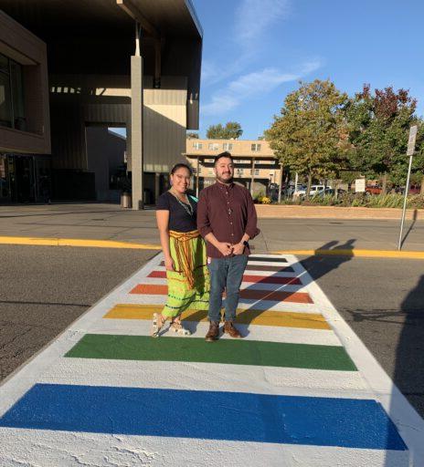 Two people standing on a LGBTQ+ themed crosswalk in front of the Dreyfus University Center.